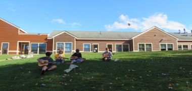 students sitting on school lawn playing guitars