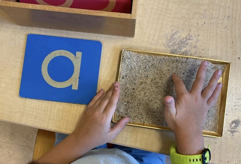 student writing letters in sand