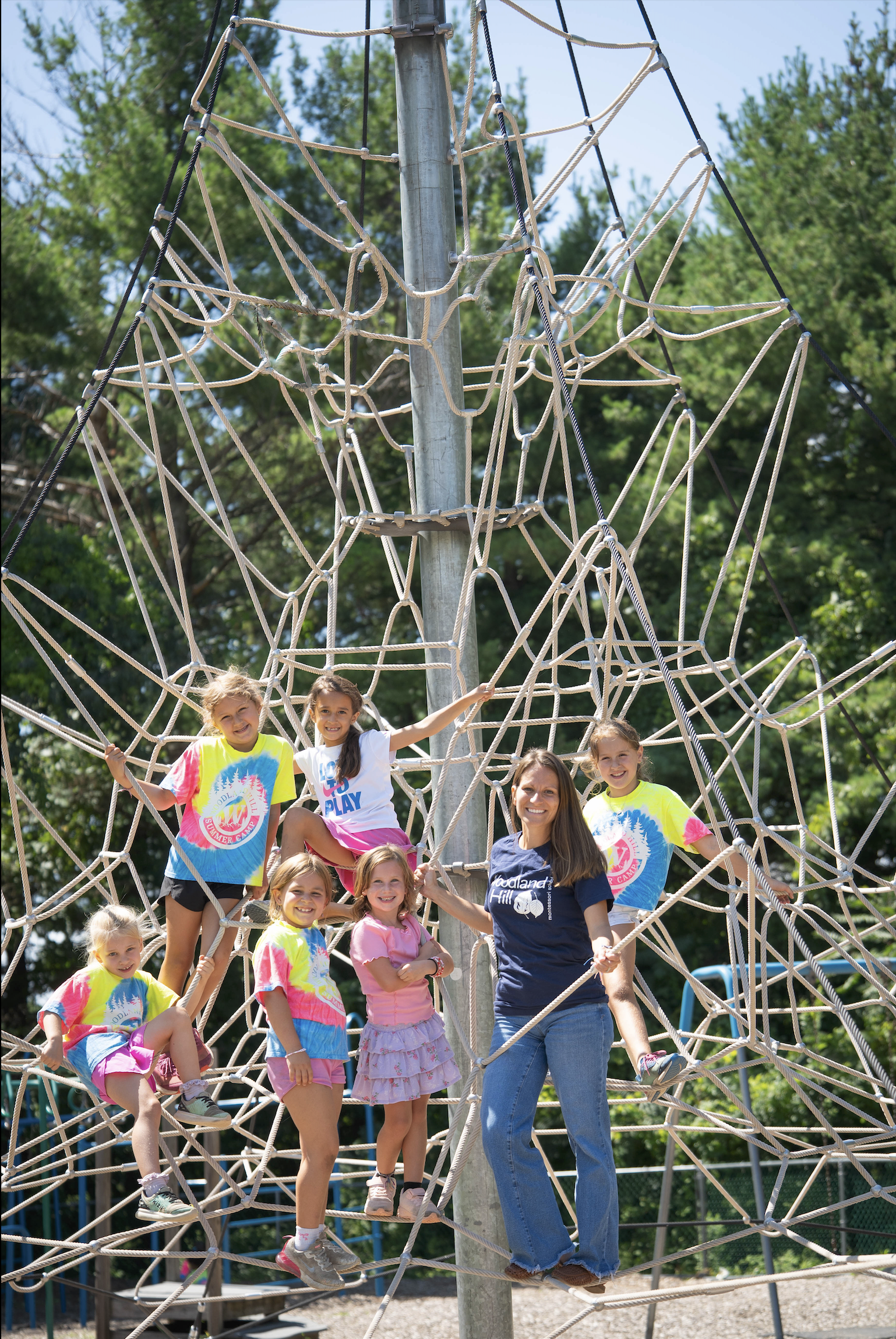 Rope-web climber with central metal support pole Children and an adult smiling and standing on a tall rope-climbing net at an outdoor playground